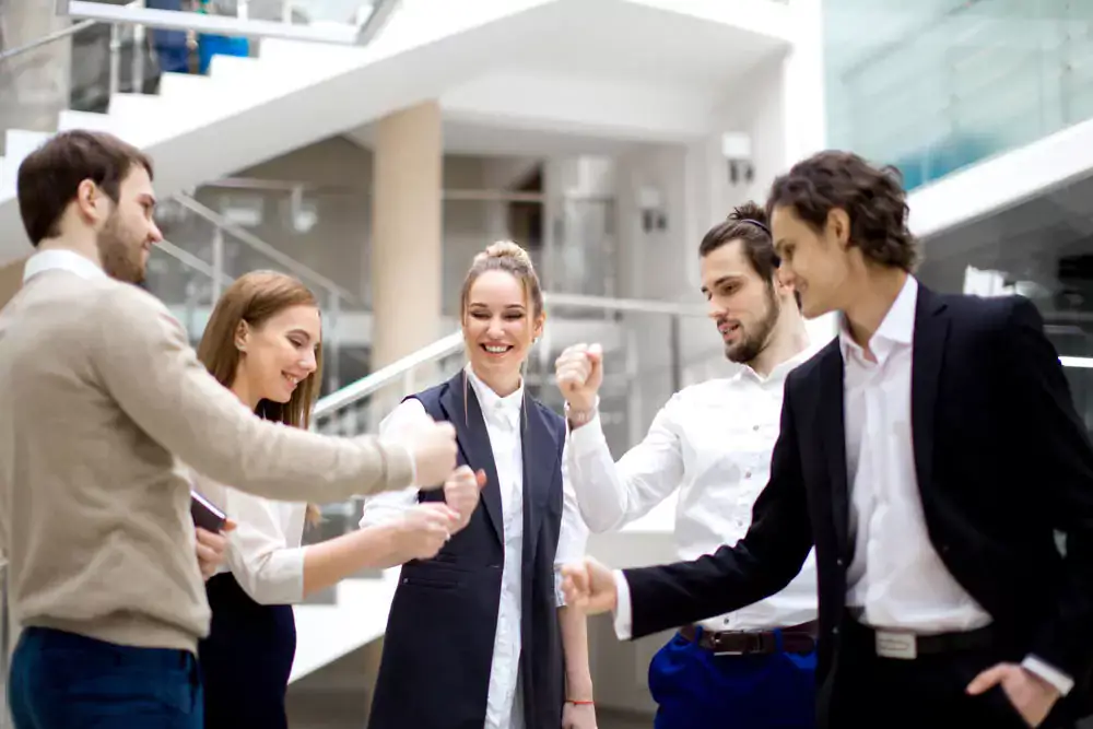 A team of employees standing in a circle inside an office atrium fist bumping.
