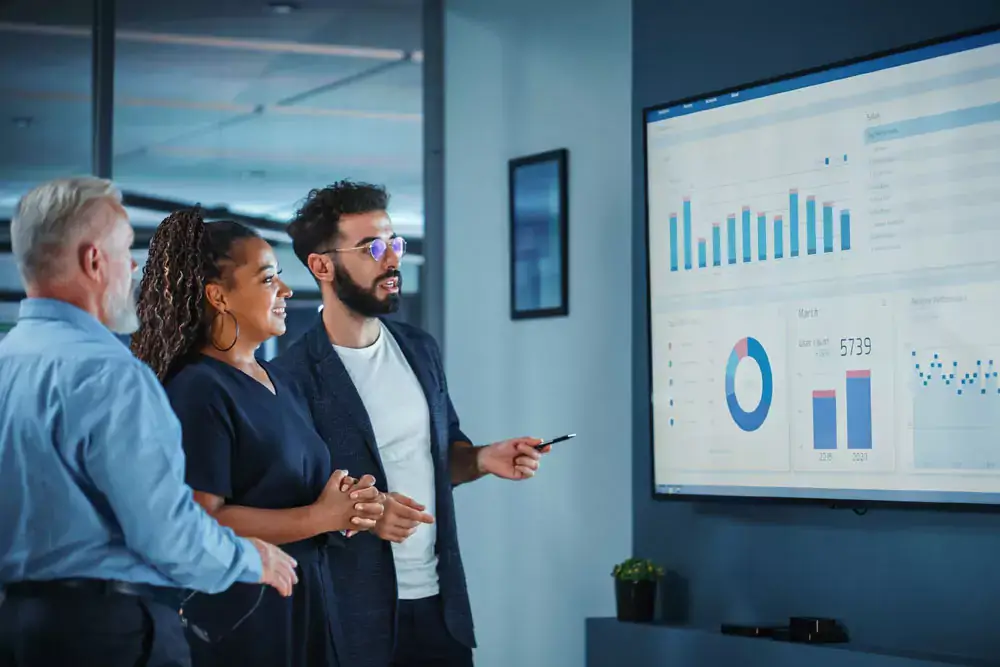 Company Operations Manager Holds Meeting Presentation with a diverse team using a TV Screen with Growth Analysis, Charts, Statistics and Data. 